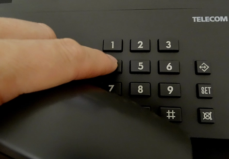 Finger tippen eine Nummer auf einem Tastentelefon.